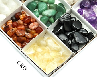 Può includere: Assortimento di pietre preziose lucide in una scatola divisa. Le pietre sono di vari colori, tra cui verde, arancione, nero, giallo e viola. La scatola è bianca e le pietre preziose sono lisce e arrotondate. Il testo "CRG" è visibile in basso a sinistra.