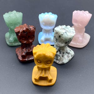 May include: Five small carved figurines of a character with a large head and a small body. The figurines are made of different types of stone, including green, blue, pink, brown, and yellow.