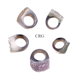 May include: Five agate rings with different crystal formations. The rings are all gray and white with some having a green hue. The rings are all different sizes and shapes. The word "CRG" is written in the center of the image.
