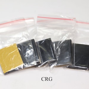 May include: Four small, black adhesive pads in individual clear plastic bags with a gold adhesive pad in one bag. The bags have red zipper closures. The text "CRG" is printed below the bags.