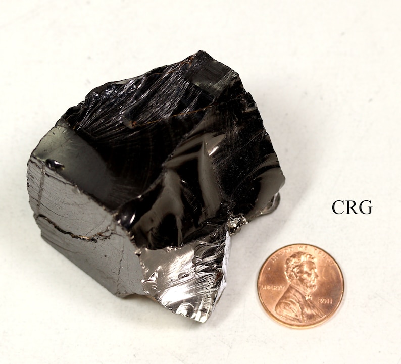May include: A large, black, obsidian rock with a shiny, glassy surface. The rock is about the size of a penny.