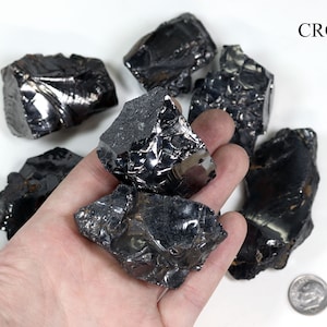 May include: A collection of six black obsidian stones of varying sizes and shapes. The stones have a shiny, glassy surface and are arranged on a white background.