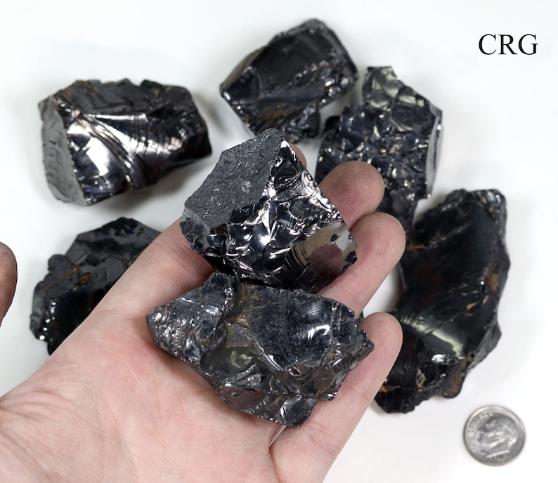 May include: A collection of six black obsidian stones of varying sizes and shapes. The stones have a shiny, glassy surface and are arranged on a white background.