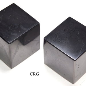 May include: Two black obsidian cubes, each with a smooth, polished surface. The cubes are slightly different in size and shape, and both have a subtle sheen.
