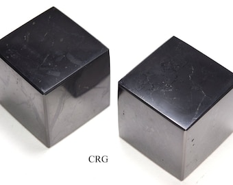 May include: Two black obsidian cubes, each with a smooth, polished surface. The cubes are slightly different in size and shape, and both have a subtle sheen.