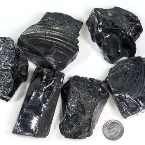 May include: A collection of six black obsidian stones, some with a striated pattern, on a white background. A US dime is included for scale.