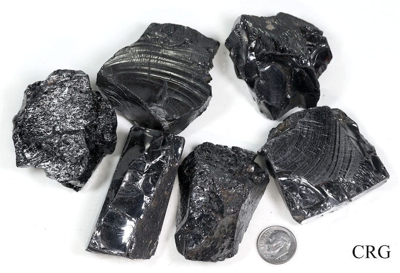 May include: A collection of six black obsidian stones, some with a striated pattern, on a white background. A US dime is included for scale.