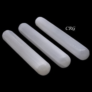 May include: Three white selenite wands, also known as selenite sticks, are arranged in a row on a black background. The wands are smooth and have a slightly striated texture.