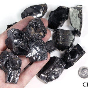 May include: A collection of black obsidian rough stones, some with a reflective surface, in a hand. A US dime is included for scale.