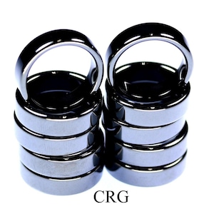 May include: A stack of six black hematite rings with a ring opening at the top. The rings are stacked on top of each other, with the top ring being the largest and the bottom ring being the smallest. The rings are all smooth and shiny.