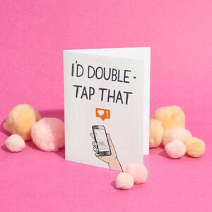 May include: White card with the text "I'd double - tap that" in black. A cartoon hand is holding a smartphone with a heart icon and the number "1" on the screen.
