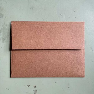 May include: A brown paper envelope, folded and sealed, with a rectangular shape. The envelope is made of a textured, matte paper material. The flap is folded over the front, creating a clean, simple design.