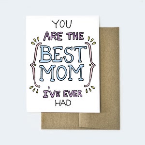 May include: A white greeting card with the text "YOU ARE THE BEST MOM I'VE EVER HAD" in a colorful, handwritten style. The card is paired with a brown envelope, perfect for Mother's Day or a special occasion.