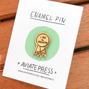 Puede incluir: Pin de esmalte dorado con fondo verde. El pin tiene forma de cinta con un c&iacute;rculo en el centro. El c&iacute;rculo dice "Voy a terapia".