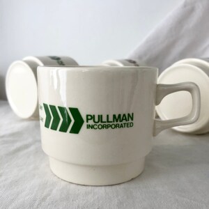 May include: White ceramic coffee mug with a green arrow design and the text "PULLMAN INCORPORATED".