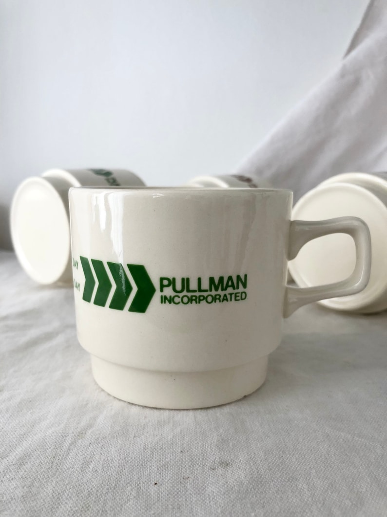 May include: White ceramic coffee mug with a green arrow design and the text "PULLMAN INCORPORATED".