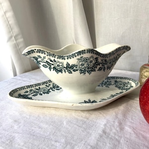 May include: A white porcelain gravy boat with a green floral design and a matching saucer. The boat has a scalloped edge and a graceful spout.