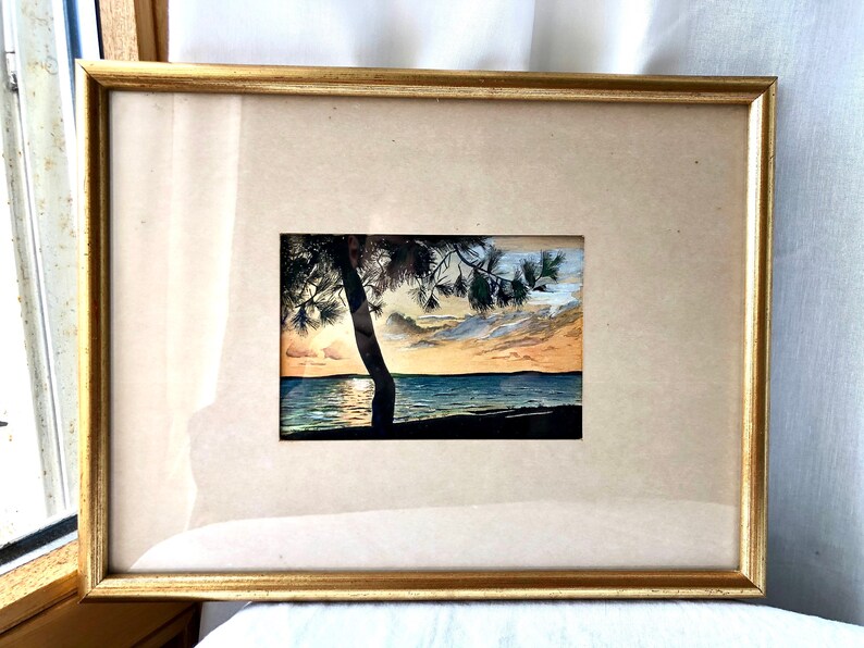 May include: Framed watercolour painting of a sunset over a lake with a silhouetted tree in the foreground.