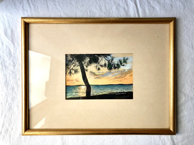 May include: A framed watercolour painting of a sunset over a lake with a silhouette of a tree in the foreground.