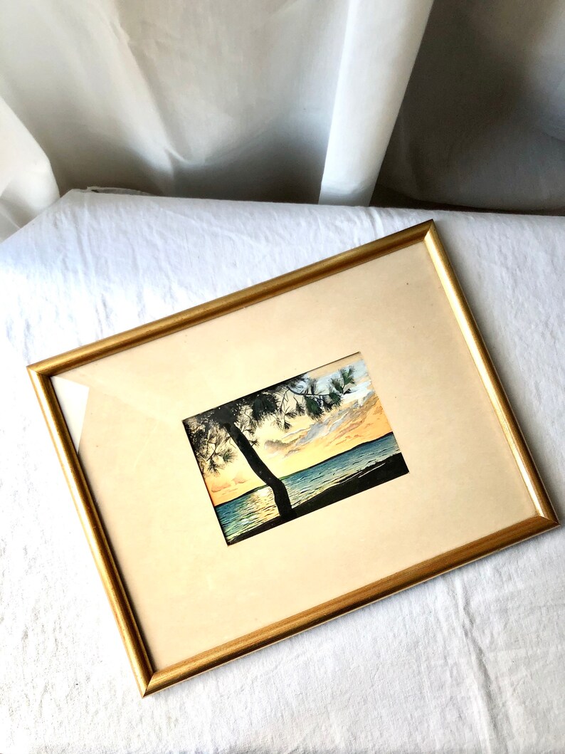 May include: A framed watercolour painting of a sunset over a body of water with a silhouette of a tree in the foreground.