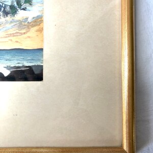 May include: A framed watercolour painting of a seascape with a pine tree in the foreground and a blue sky with clouds in the background.