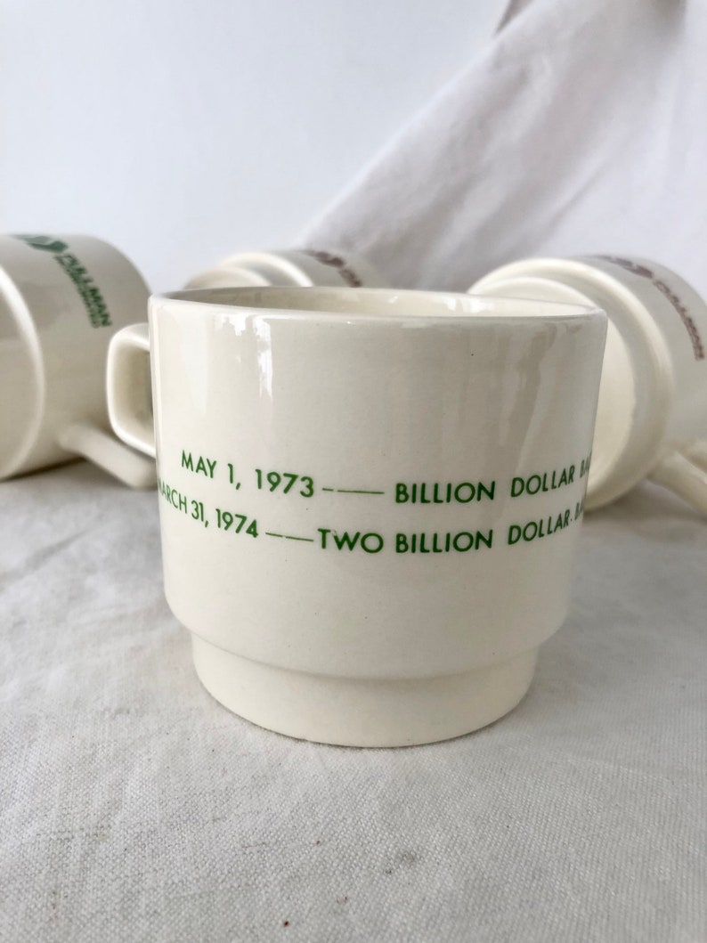 May include: White ceramic coffee mug with green text that reads "May 1, 1973 - Billion Dollar Sales - March 31, 1974 - Two Billion Dollar Sales".
