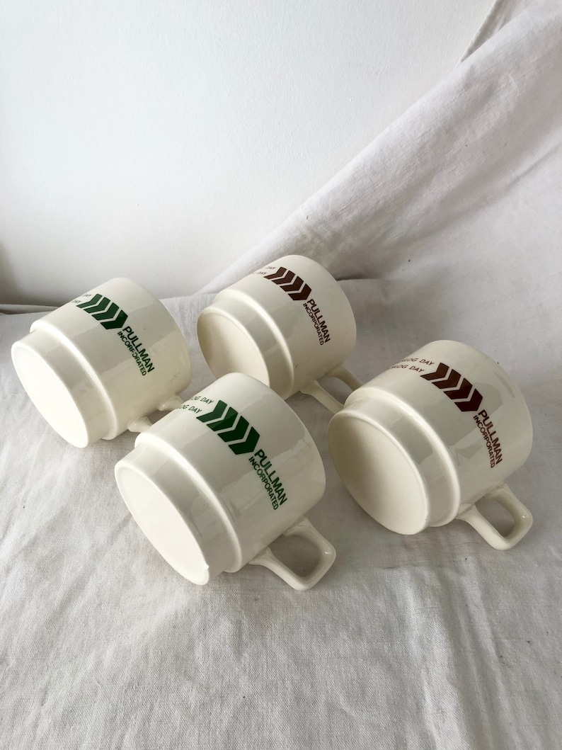 May include: Four white ceramic mugs with a green and brown logo that reads "Pullman Incorporated".