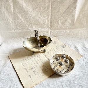 May include: A silver serving dish with a handle and a silver tray with six small glass salt shakers on a sheet of paper with handwritten text.