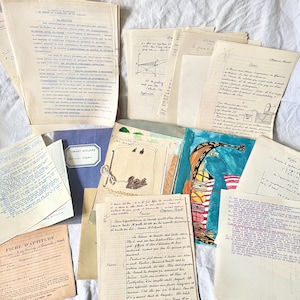 May include: A collection of vintage documents, including handwritten notes, printed papers, and a blue school notebook. The papers vary in size and are scattered across a white surface. Some documents feature illustrations and text in French.