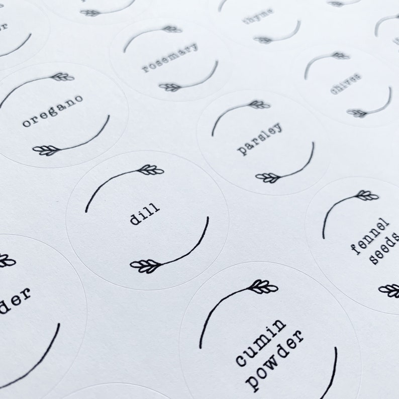 Op de afbeelding: Een set witte ronde labels met zwarte tekst en een eenvoudige tekening van een tarwehalm. De labels bevatten de woorden: oregano, rozemarijn, peterselie, dille, venkelzaad, komijnpoeder.
