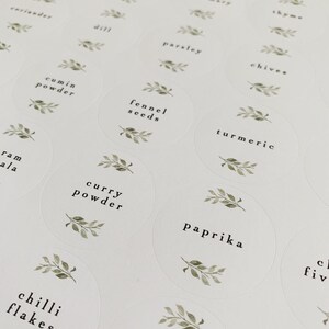 K&ouml;nnte beinhalten: Ein Satz runder wei&szlig;er Etiketten mit gr&uuml;nen Aquarellbl&auml;ttern und schwarzem Text. Die Etiketten sind f&uuml;r Gew&uuml;rze und Kr&auml;uter, darunter Koriander, Petersilie, Schnittlauch, Kreuzk&uuml;mmelpulver, Fenchelsamen, Kurkuma, Currypulver, Paprika, Chiliflocken und Dill.