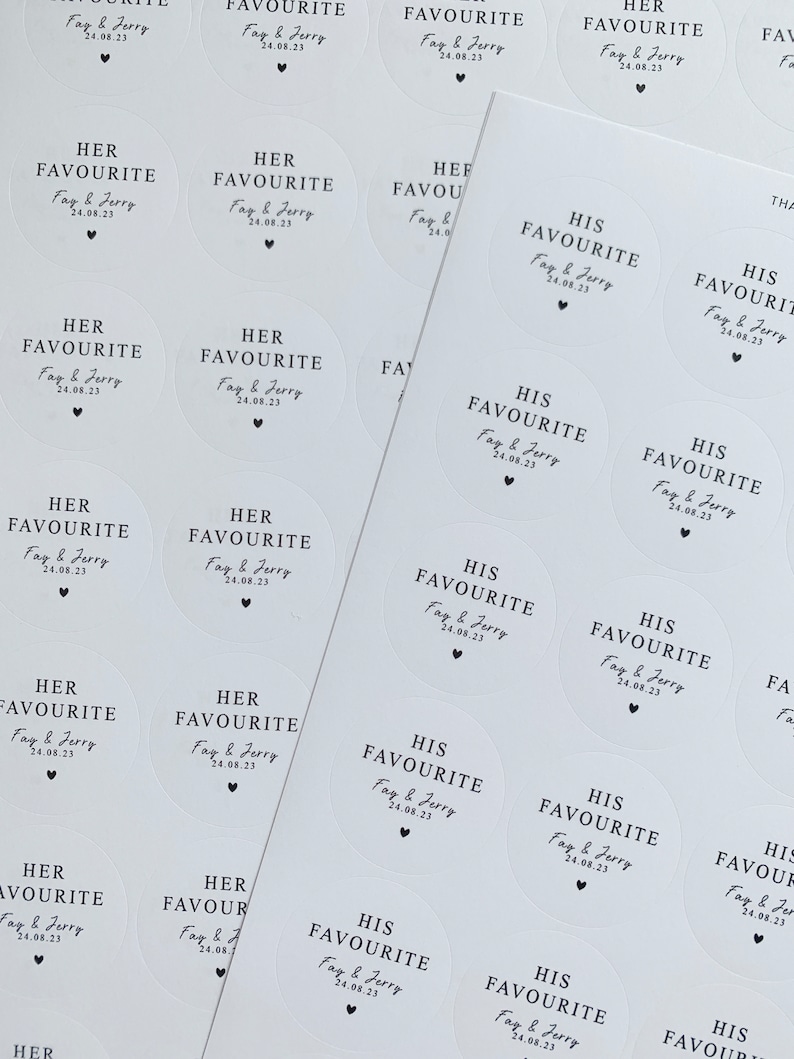 May include: Sheets of white, circular stickers with black text. The stickers read "HER FAVOURITE" and "HIS FAVOURITE" with a date and a heart symbol. The stickers are for a wedding or special event.