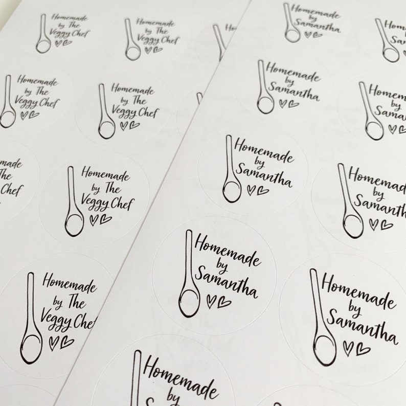 K&ouml;nnte beinhalten: Ein Blatt wei&szlig;es Aufkleberpapier mit mehreren runden Aufklebern, auf denen der Text "Homemade by The Veggy Chef" und eine Zeichnung eines Holzl&ouml;ffels gedruckt ist. Andere Aufkleber zeigen den Text "Homemade by Samantha" mit einer Zeichnung eines Holzl&ouml;ffels.