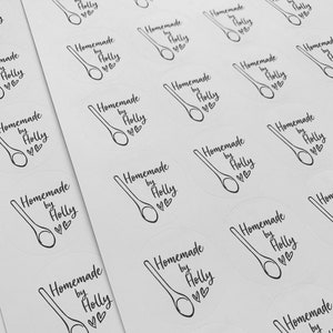 K&ouml;nnte beinhalten: Ein Blatt mit wei&szlig;en runden Aufklebern mit schwarzem Text und einer Zeichnung eines Holzl&ouml;ffels. Der Text auf den Aufklebern lautet "Homemade by Holly" mit zwei Herzen.
