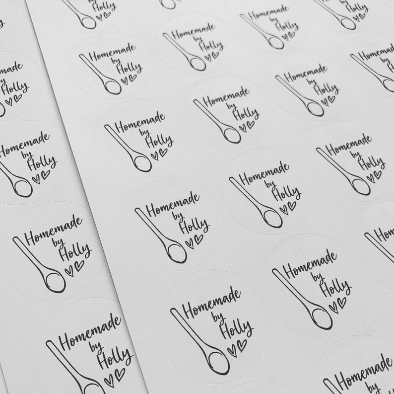 K&ouml;nnte beinhalten: Ein Blatt mit wei&szlig;en runden Aufklebern mit schwarzem Text und einer Zeichnung eines Holzl&ouml;ffels. Der Text auf den Aufklebern lautet "Homemade by Holly" mit zwei Herzen.