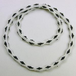 May include: A black and white beaded necklace with a diamond pattern. The necklace is made of small, round beads and is approximately 40 inches long.