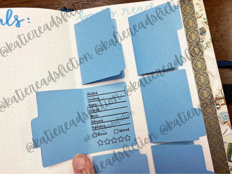 May include: Blue index cards with tabs for a book journal. The cards have lines for tracking book details, including "Started", "Finished", "Pages", "Format", "Genre", "Released", "Published", "Review", and "Spread".