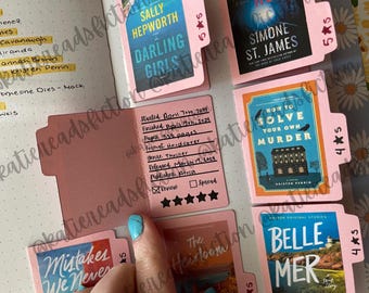 May include: A close-up of a pink book tracker with several book covers visible. The book tracker has a five-star rating system and space to write the book title, author, start date, finish date, pages, format, genre, release date, publisher, and review. The book covers are for "Darling Girls" by Sally Hepworth, "How to Solve Your Own Murder" by Kristen Brown, "Belle Mer" by  Simone St. James, and "The Heirloom" by