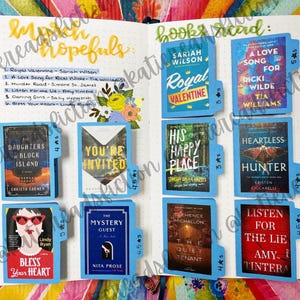 May include: A close-up of a book journal with blue tabs and book covers. The journal is open to a page with a list of books read and a list of books to read. The book covers are colorful and feature a variety of genres. The tabs are labeled with star ratings.