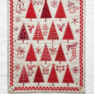 May include: A red and white embroidered Christmas quilt with the text "Merry Little Christmas" and "Kathy Schmitz". The quilt features a variety of Christmas trees, ornaments, and other festive designs. It measures 13 inches by 16 1/2 inches.