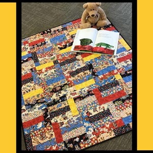 May include: A patchwork quilt in vibrant colours, with red, blue, and yellow squares. A teddy bear and an open book with illustrations of a turtle and a crocodile are on the quilt. The word "Playdate" is at the top. The quilt is a child's item.