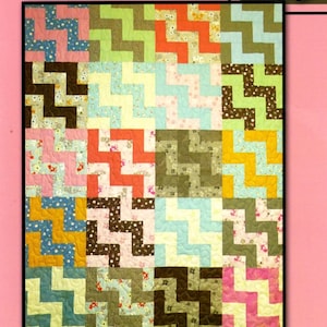 May include: A colorful quilt with a zig-zag pattern in various colors, including pink, green, blue, and brown. The quilt is labeled "SOCIAL CLIMBER" and "Villa Rosa Designs". A pink rose is in the upper right corner.