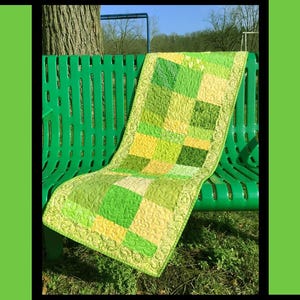 Może przedstawiać: Zielono-żółta patchworkowa kołdra z napisem "Clover" i grafiką czterolistnej koniczyny. Kołdra jest narzucona na zieloną ławkę. Widoczny jest również tekst "Tricia Lynn Maloney Orphan Quilt Designs For Villa Rosa Designs".