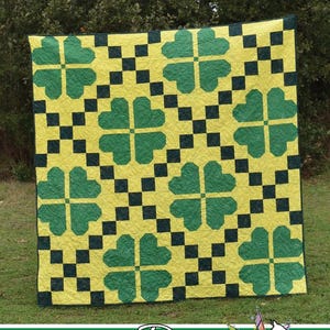 May include: A yellow quilt with a repeating pattern of green shamrocks and black squares. The words "PINCH ME" are at the top, and the Running Doe Quilts logo is at the bottom. The quilt is displayed outdoors.