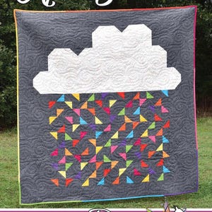 May include: A handmade quilt with a dark gray background features a white cloud and colorful triangle rain. The quilt has a rainbow border and the text "April Showers" at the top. The quilt is made by Running Doe Quilts.
