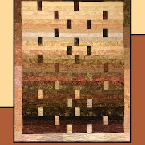 May include: A quilt with the text "Fudge Sundae" at the top. The quilt features horizontal stripes in shades of brown, tan, and cream, with rectangular accents. The quilt is designed by Molly Cook for Villa Rosa Designs.