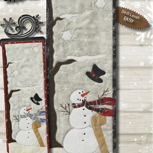 May include: A fabric panel featuring a snowman with a carrot nose, wearing a scarf and hat, with the text "WINDY WINTER". The panel measures 6.5" x 18" and has an easy skill level.