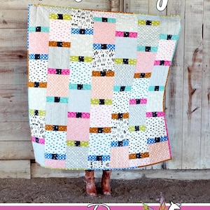 Pode incluir: Um edredom colorido com a palavra "Flutterby" em escrita. O edredom apresenta um design de patchwork com vários padrões e cores, incluindo rosa, azul e preto. O logotipo Running Doe Quilts está na parte inferior.