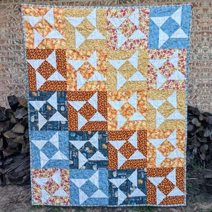 May include: A patchwork quilt with a windmill pattern in shades of orange, yellow, blue, and white. The quilt features the text "Tall Windmills" at the top and "Sewl Sister for Villa Rosa Designs" at the bottom.