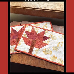May include: Two pressed leaf snack mats with a red and orange leaf design on a white background. The mats are on a wooden surface. The text "Pressed Leaf Snack Mat" is at the top of the image. The text "Tricia Lynn Maloney Orphan Quilt Designs for Villa Rosa Designs" is at the bottom of the image.